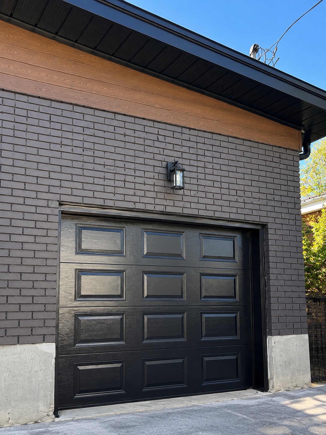 Porte de garage peinte en noir sur façade de brique grise